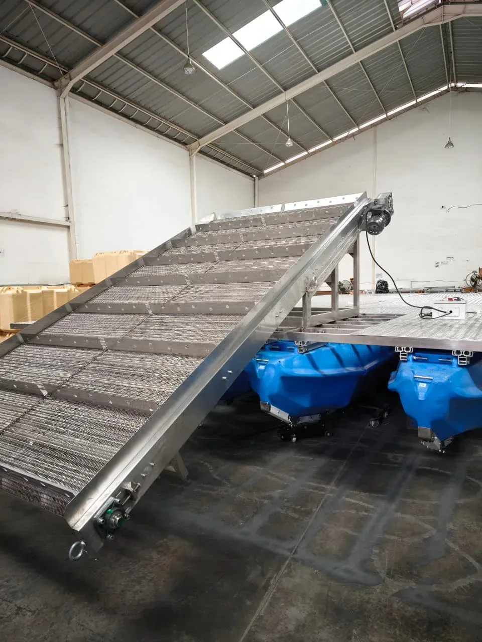 Conveyor sampah apung berbahan logam dirakit di atas ponton biru di dalam workshop