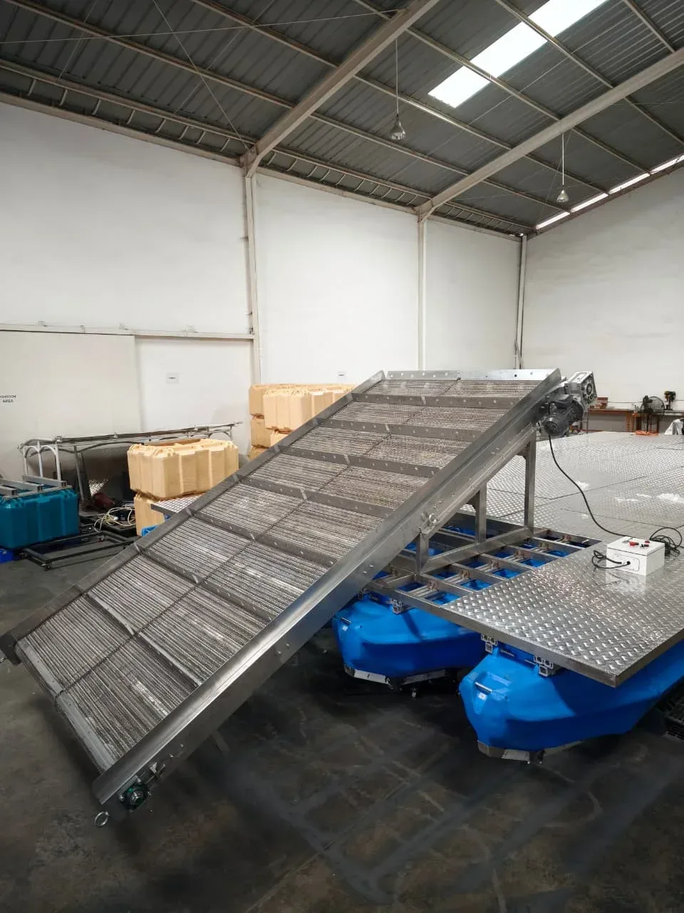 Rangka conveyor miring dan dek berlubang di atas ponton biru saat perakitan di workshop
