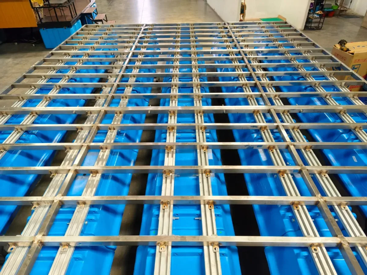 Rangka aluminium berpola grid terpasang di atas baris ponton biru di workshop