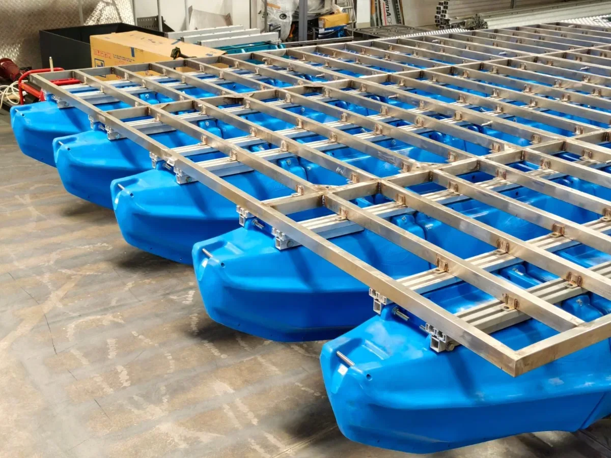 Rangka aluminium dipasang di atas deretan ponton apung biru di dalam workshop