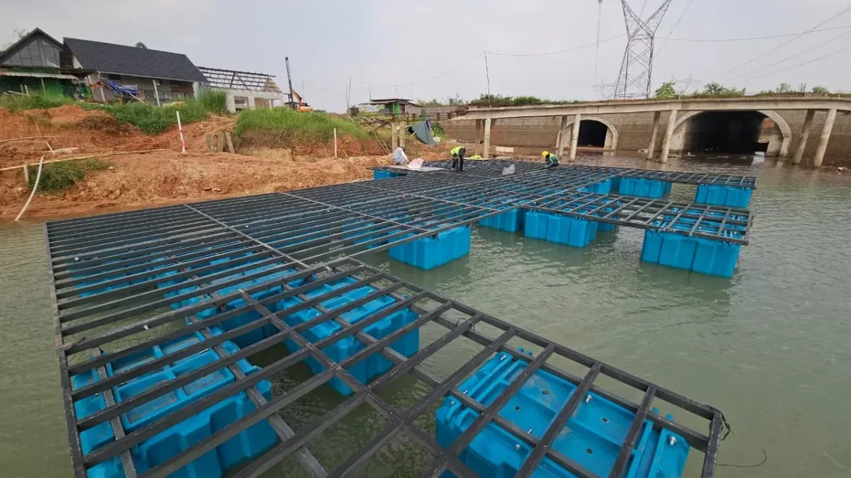 Rangka besi hitam berpola grid dipasang di atas ponton biru saat pemasangan dermaga
