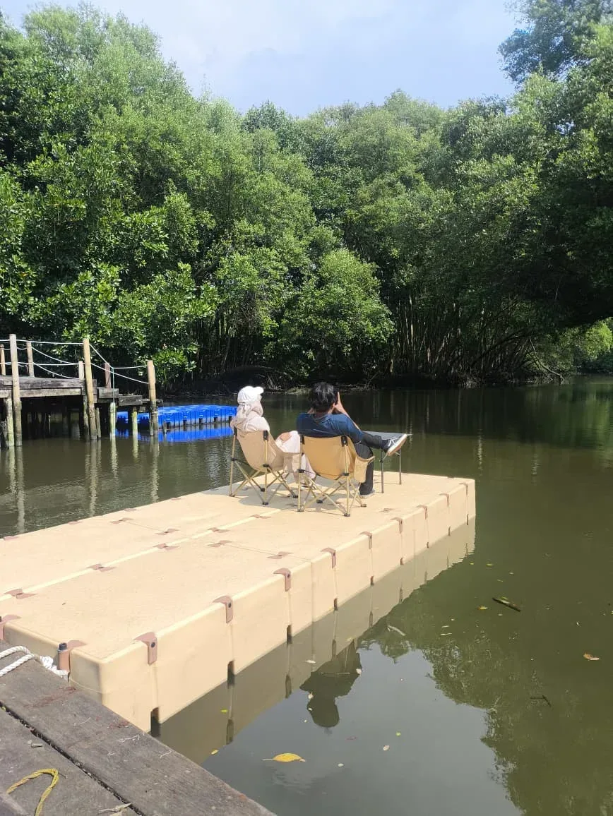 Dua orang duduk santai di platform Nusa Dock krem di tepi hutan mangrove